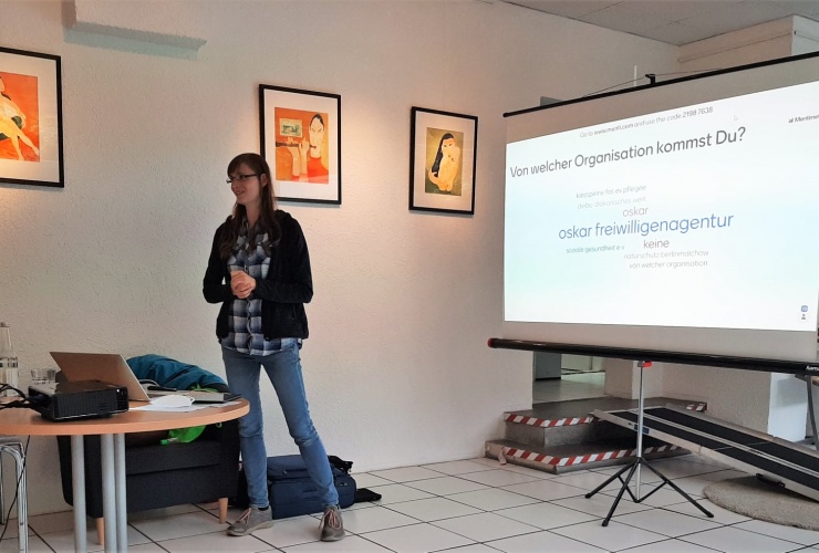 Auf dem Bild sieht man Petra von der Digitalen Nahcbarschaft. Sie steht vor einer Leinwand und hält eine Präsentation.